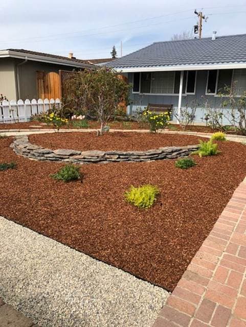 Landscaped front yard with stone garden, mulch, and flowering plants in a residential area.
