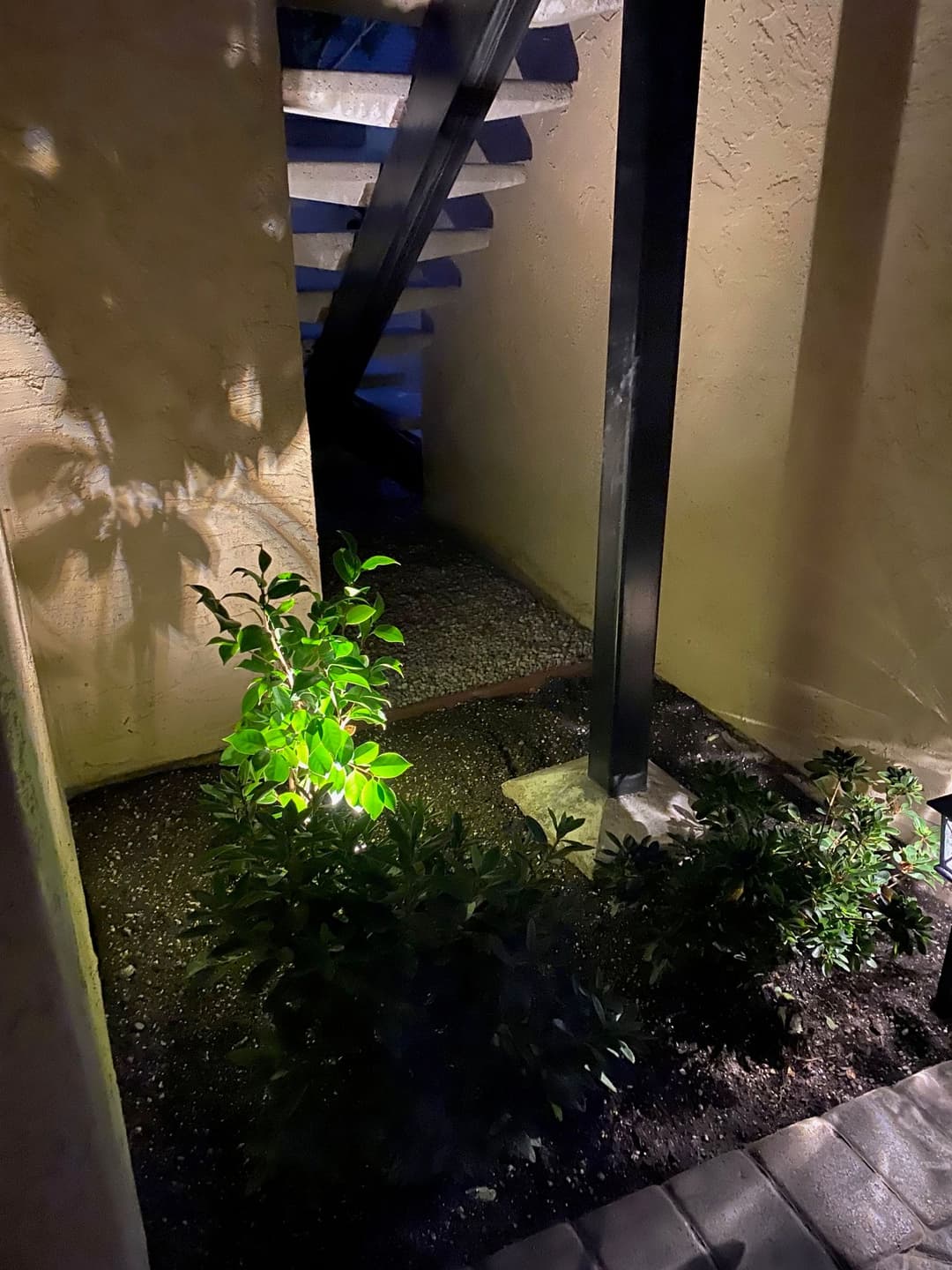 Illuminated garden path leading to spiral staircase between two walls at night.