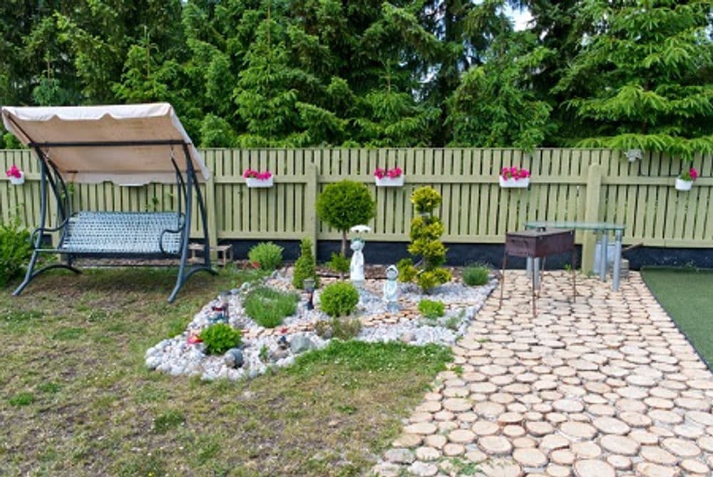 Garden with swing chair, stone path, and decorative plants against a green fence.