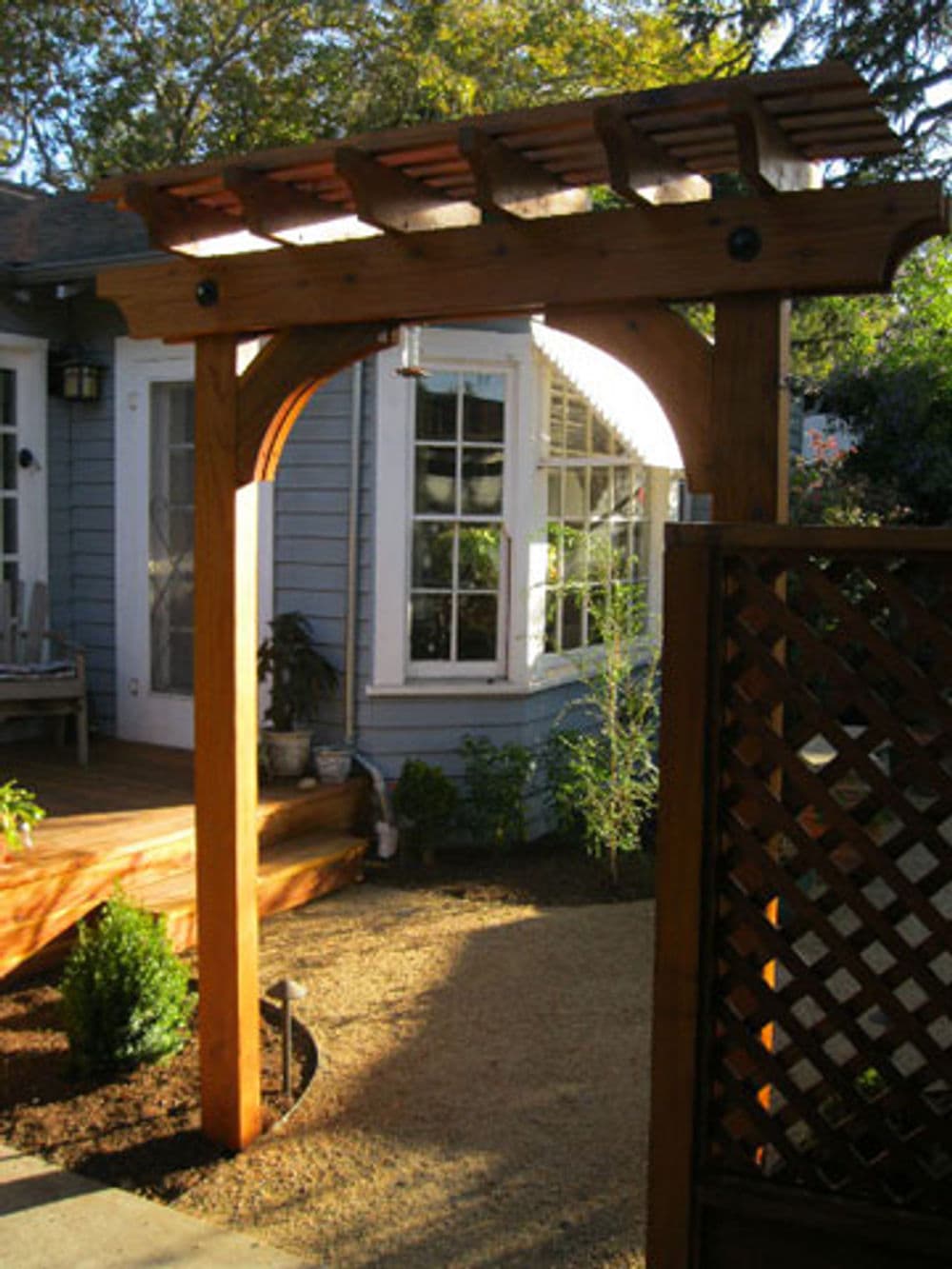 Wooden garden arbor with lattice design, leading to a landscaped patio area.