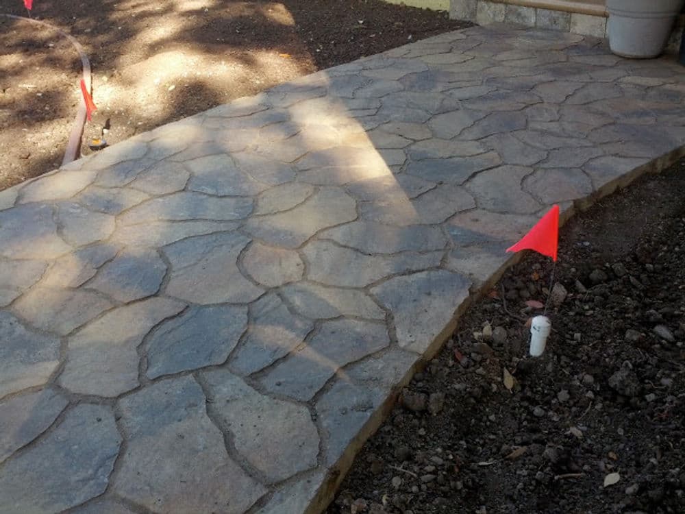 Stone walkway installation with red flags marking boundaries and unfinished landscaping.