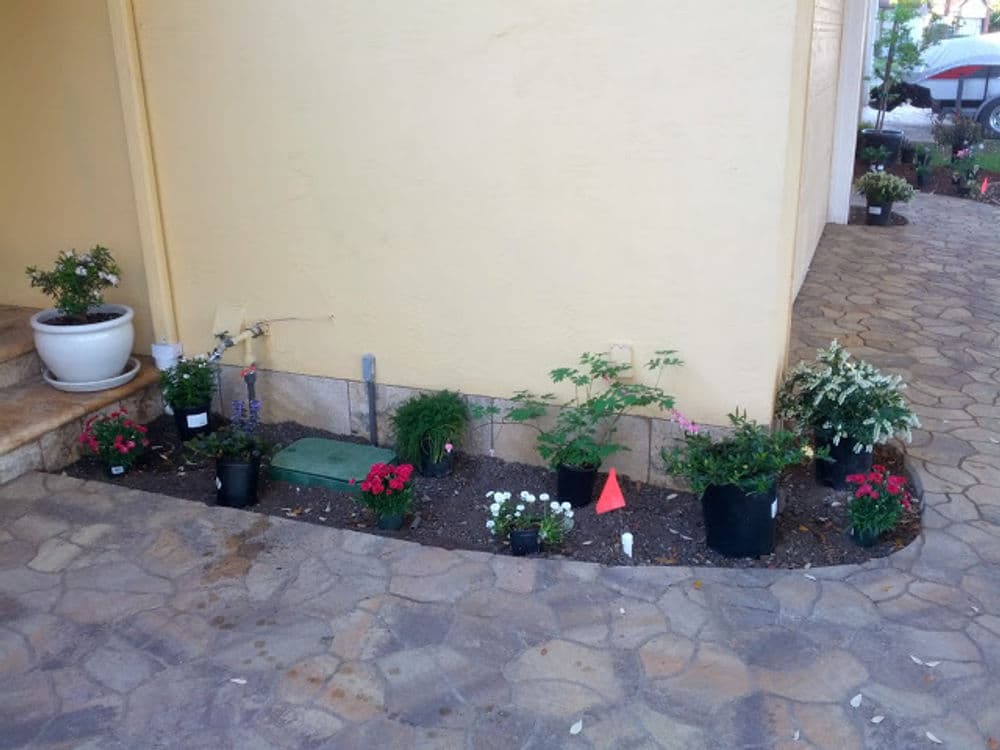 Colorful flower bed with potted plants and decorative stones by a house entrance.