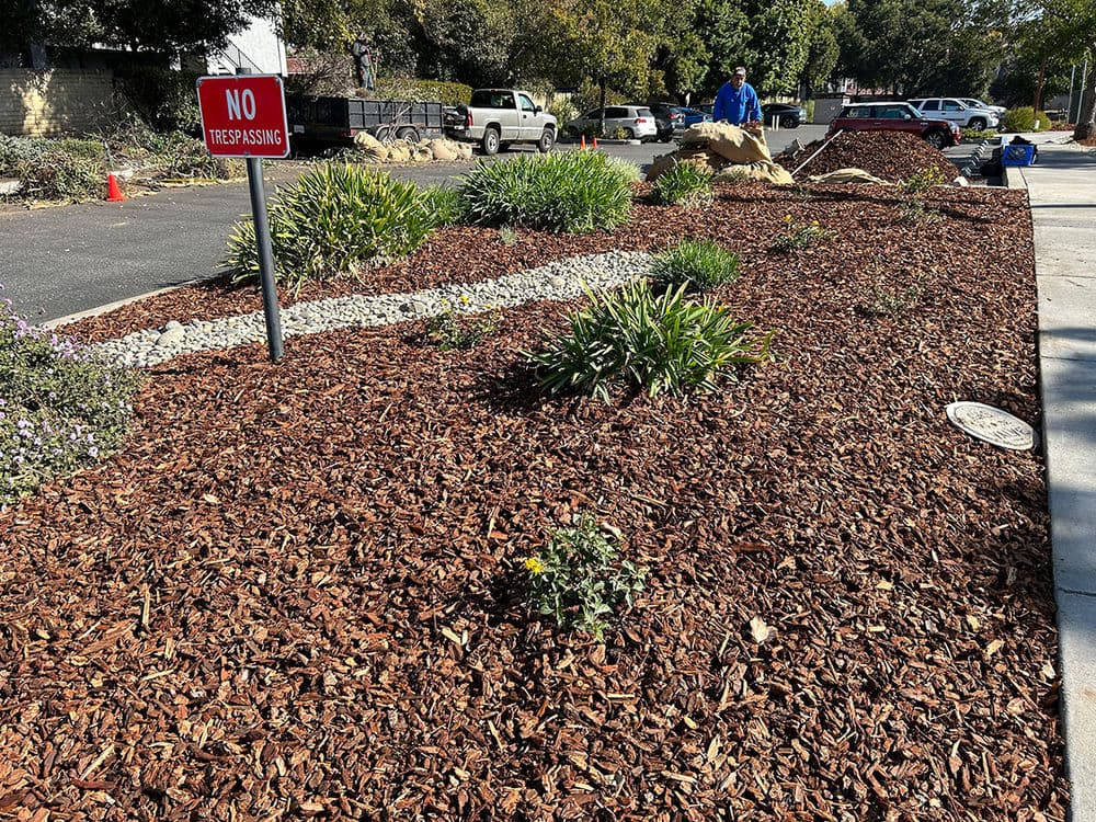 Lush landscaping with mulch, plants, and a "No Trespassing" sign in a residential area.