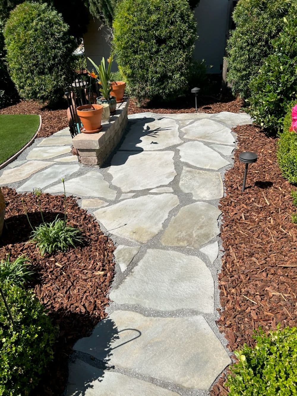 Stone pathway through a landscaped garden featuring plants and decorative lighting.