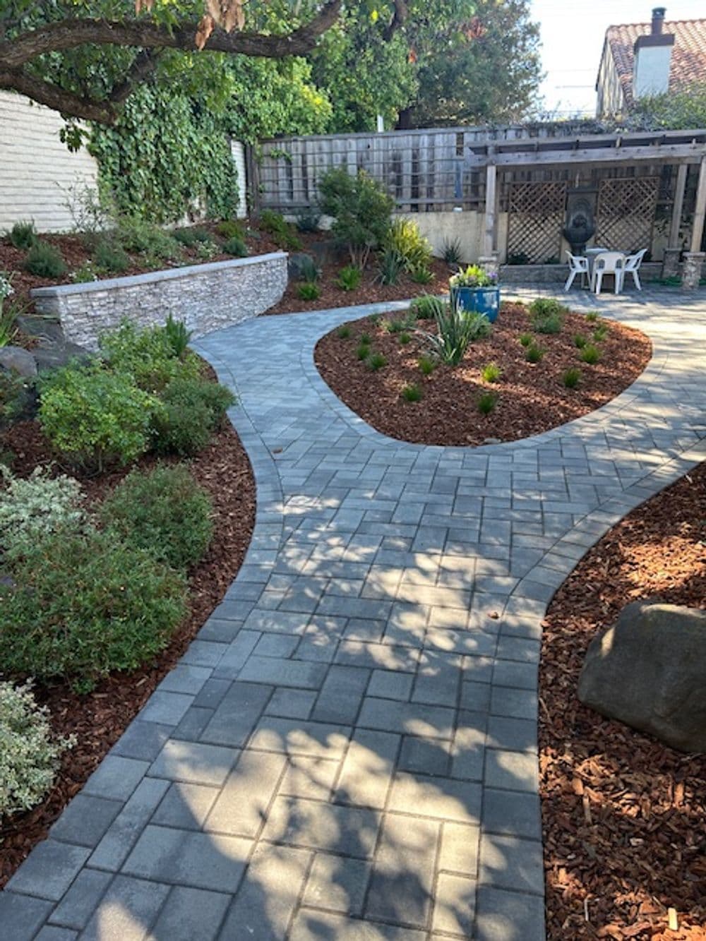 Lush garden pathway with stone pavers, landscaped beds, and seating area under a pergola.